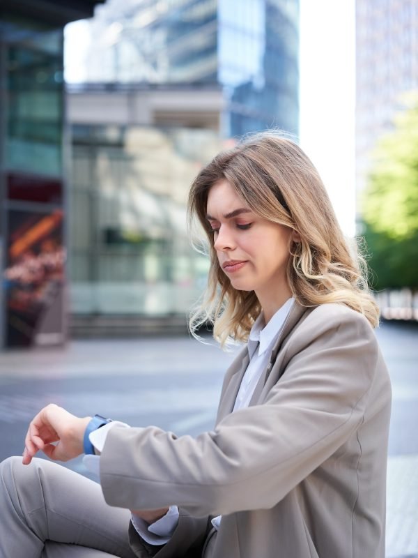 frowning-businesswoman-in-suit-looking-at-her-digital-watch-with-disappointed-face-annoyed